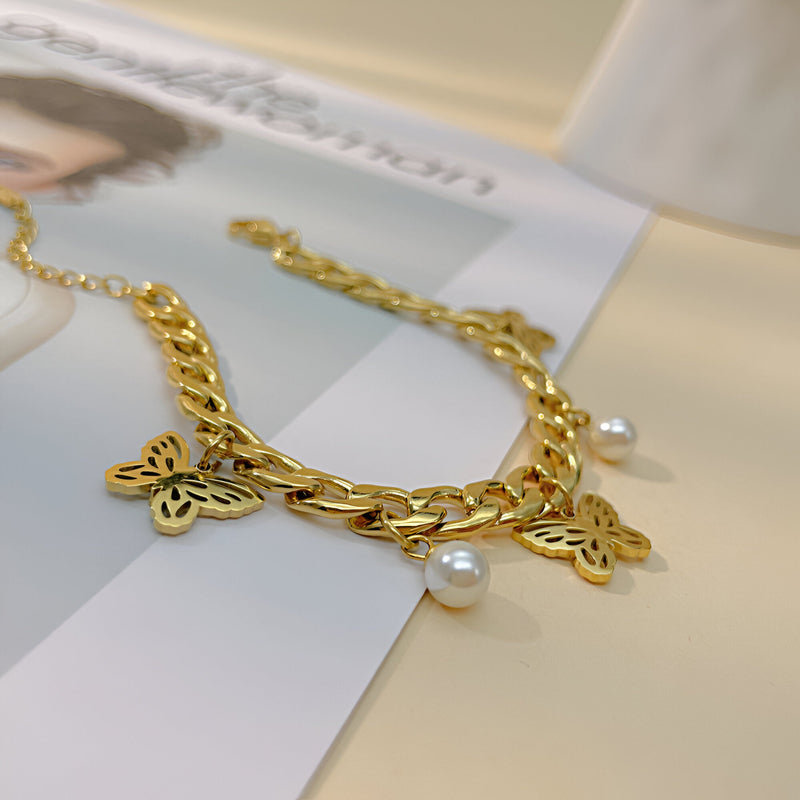 Bracelet femme en acier inoxydable doré avec trois papillons sculptés et deux perles blanches pendentifs.