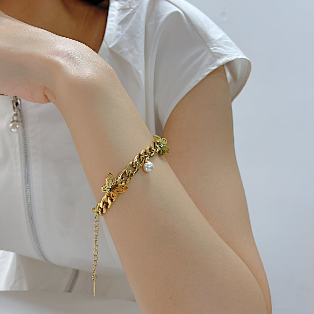 Bracelet en acier inoxydable doré avec trois papillons sculptés et une perle pendante.