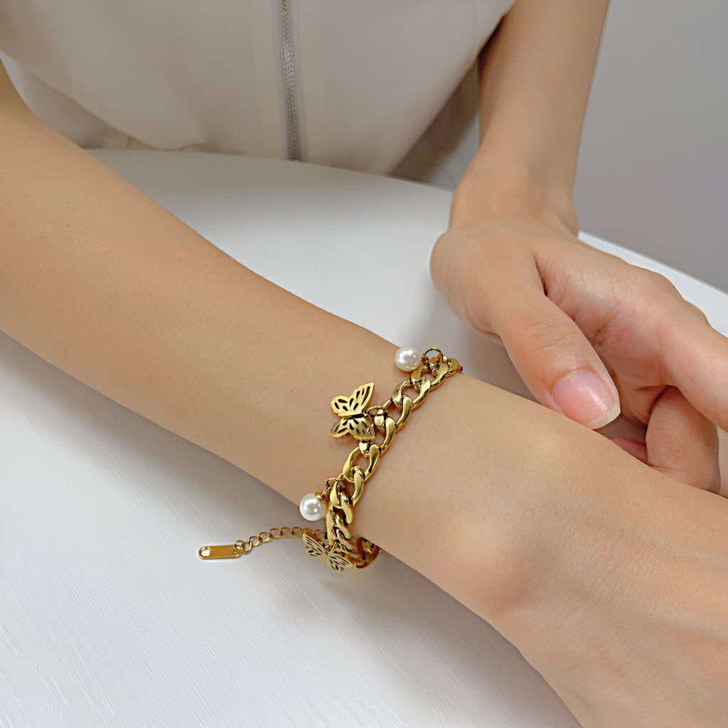 Bracelet femme en acier inoxydable doré avec trois papillons sculptés et perle sur chaîne élégante.