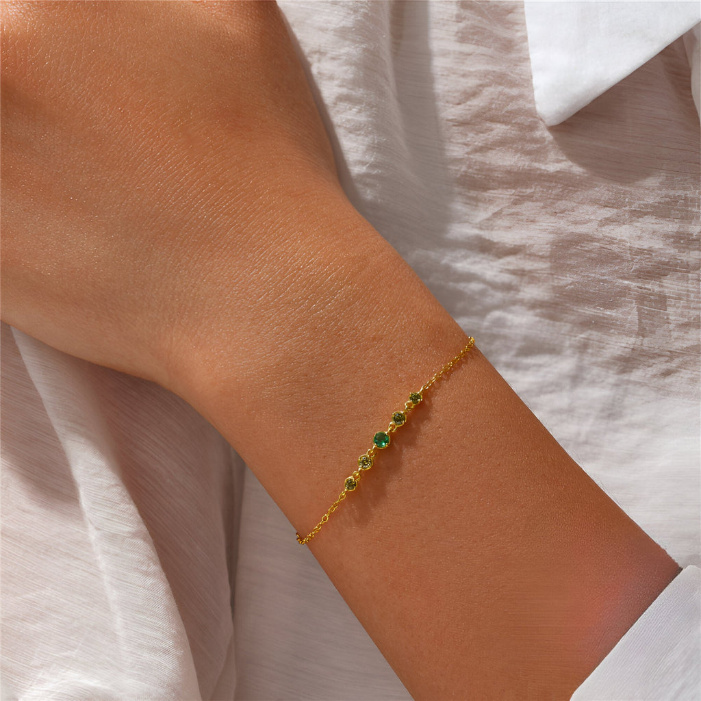Bracelet fin en argent sterling avec zircons verts sur chaîne délicate portée au poignet féminin.