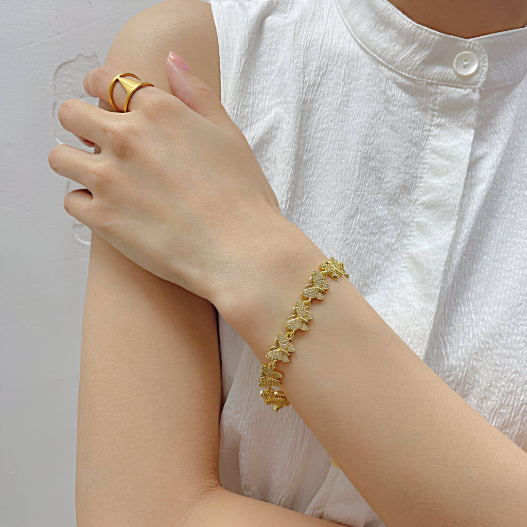 Bracelet fin en cuivre doré orné de multiples papillons sertis de zirconium sur poignet féminin.