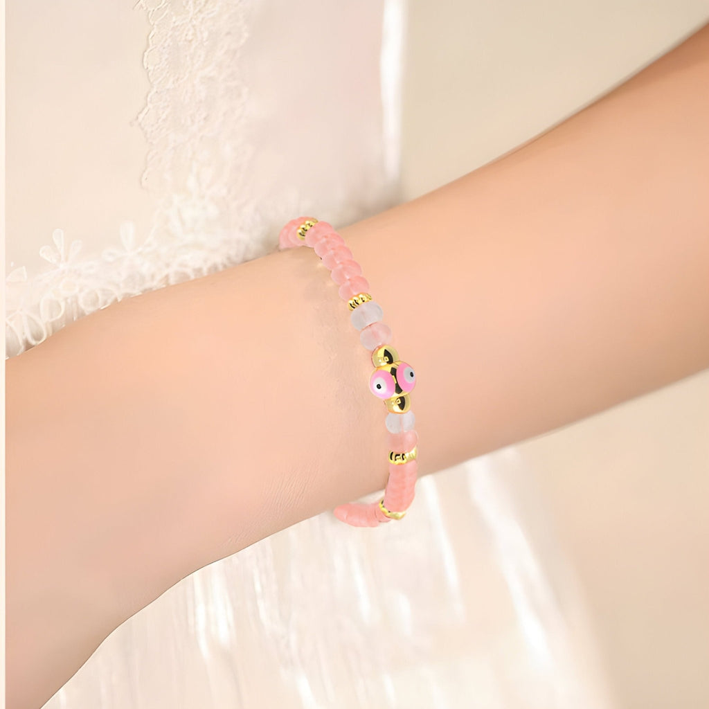 Bracelet rose en quartz avec perles et petit œil noir et blanc sur poignet féminin.