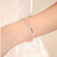 Bracelet rose en quartz avec perles et petit œil noir et blanc sur poignet féminin.