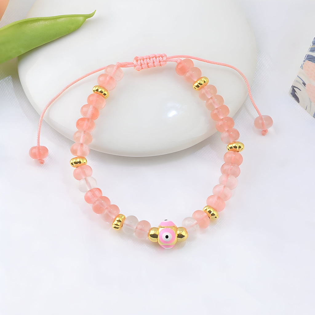 Bracelet ajustable en quartz rose avec perles dorées et petit œil rose au centre.