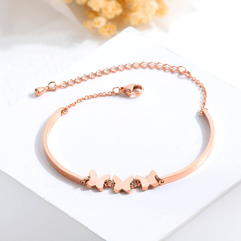 Bracelet en acier inoxydable or rosé avec cinq papillons alignés et chaîne réglable.
