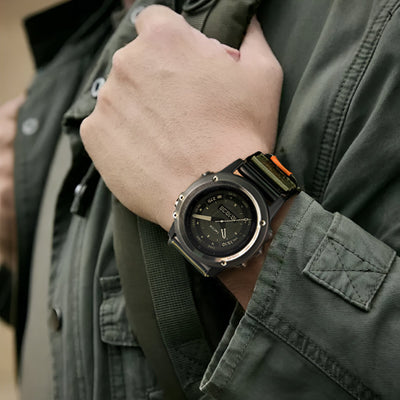 Bracelet montre connecté nylon kaki avec attache velcro noire, style tactique, porté au poignet.