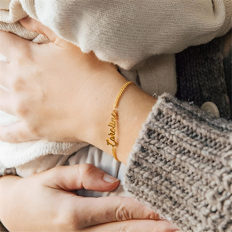 Bracelet prénom ajustable en acier inoxydable doré avec lettres script personnalisées porté au poignet féminin.