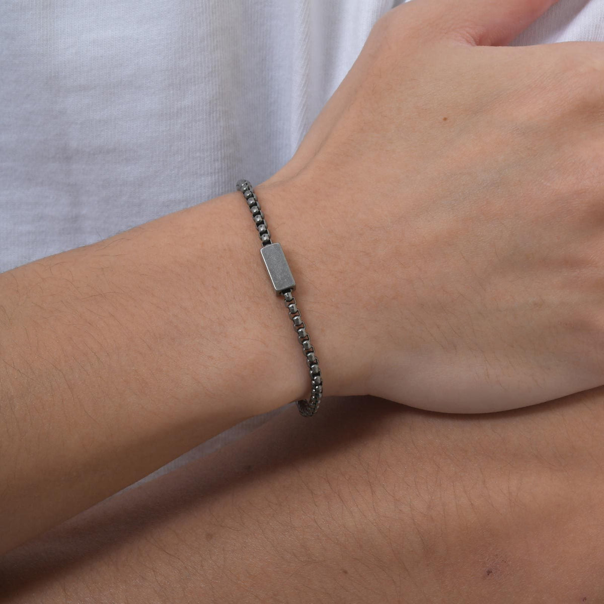 Bracelet prénom en acier inoxydable gris foncé avec maille vénitienne fine et fermoir sécurisé porté au poignet.