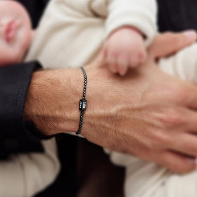 Bracelet prénom personnalisé noir en maille vénitienne fine avec plaque gravée en acier inoxydable sur poignet masculin.