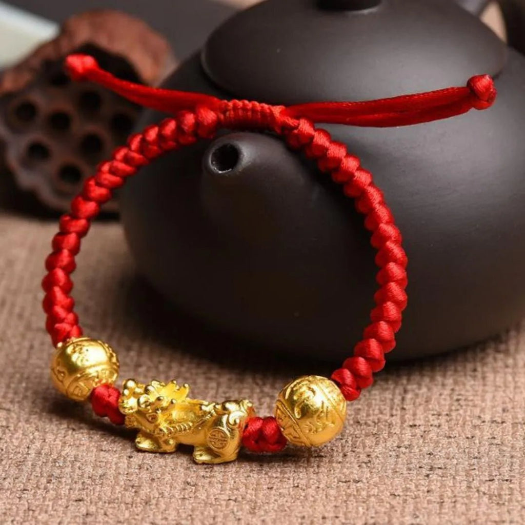 Bracelet tibétain en fil rouge ciré tressé avec breloques dorées Pi Xiu et sphères porte-bonheur.
