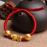 Bracelet tibétain en fil rouge ciré tressé avec breloques dorées Pi Xiu et sphères porte-bonheur.