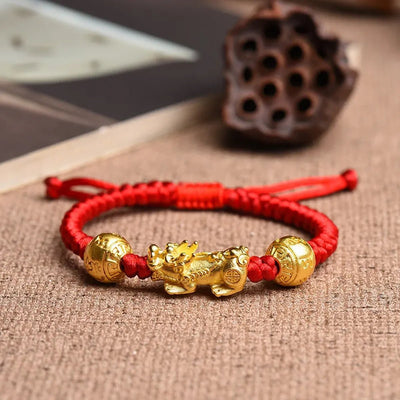 Bracelet tibétain en fil rouge ciré avec pendentif Pi Xiu doré et perles décoratives dorées.