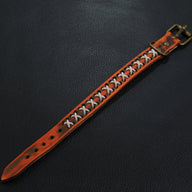 Bracelet en cuir orange avec motif cordes croisées blanches et boucle en métal doré.