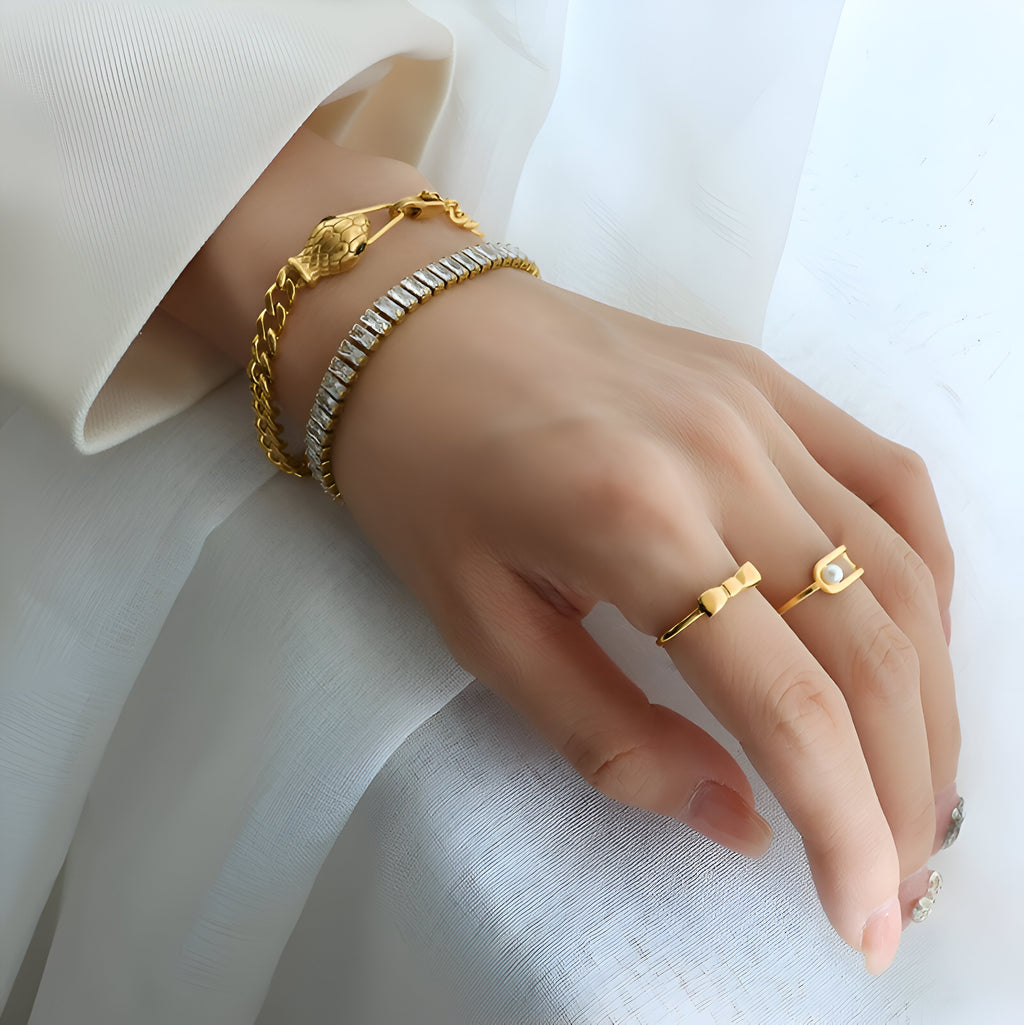 Bracelet serpent plaqué or 18 carats avec yeux verts porté avec un bracelet chaîne dorée et deux bagues fines or sur main.