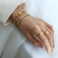 Bracelet serpent plaqué or 18 carats avec yeux verts porté avec un bracelet chaîne dorée et deux bagues fines or sur main.