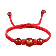Bracelet en nylon fil rouge avec perles rouges et signe du zodiaque chinois doré au centre.