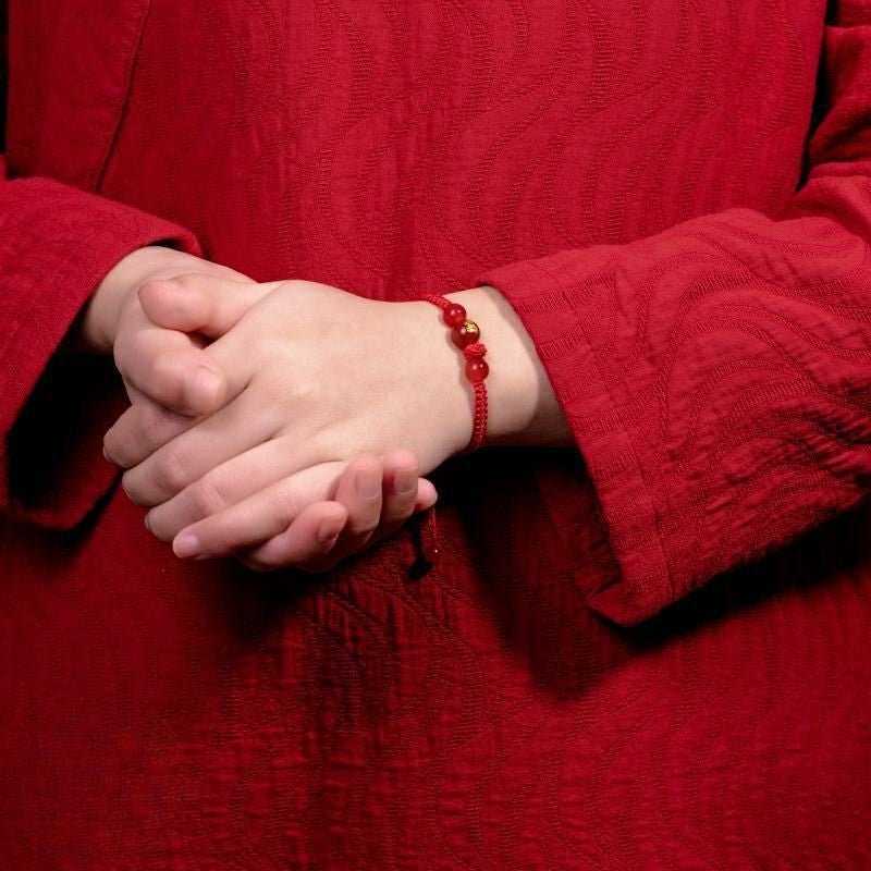 Bracelet en nylon rouge avec perles sculptées signe zodiac chinois porté au poignet sur chemise rouge.