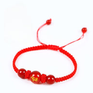 Bracelet en nylon rouge tressé avec perle centrale rouge ornée d’un symbole doré du zodiaque chinois.