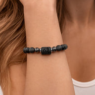 Bracelet élastique mixte en perles noires, pierres de lave texturées, hématite brillante et perle centrale carrée gravée du.