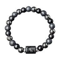 Bracelet élastique avec perles noires mates, pierres de lave texturées et hématite brillante, avec un pendentif zodiacal.