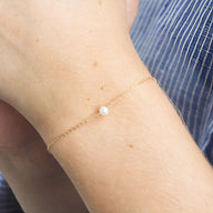 Bracelet fin en acier inoxydable doré avec perle blanche centrale délicate.