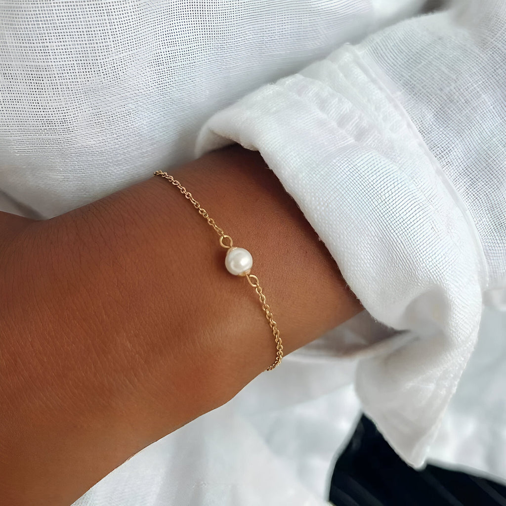 Bracelet délicat en acier inoxydable doré avec perle centrale ronde, style minimaliste.