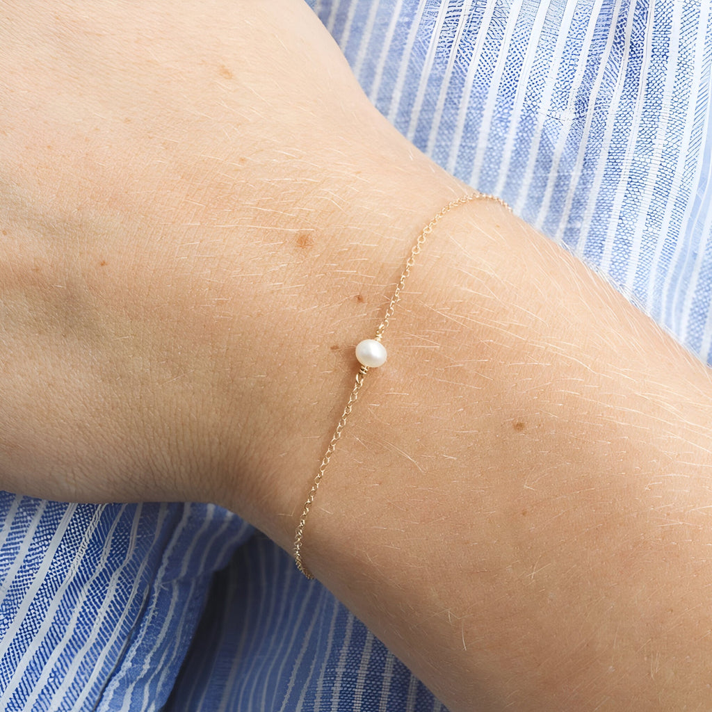 Bracelet fin en acier inoxydable doré avec perle centrale blanche élégante.
