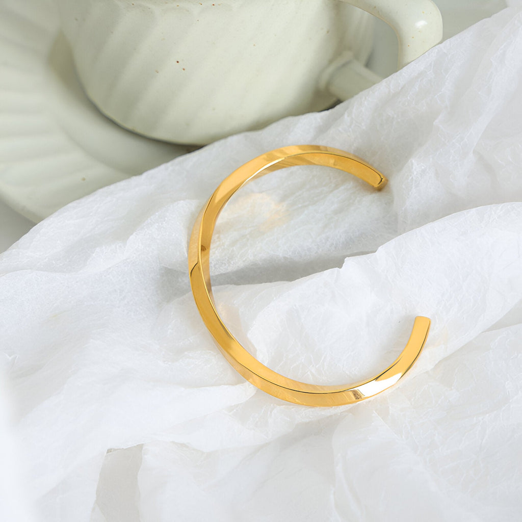 Bracelet jonc ouvert en titane plaqué or brillant au design minimaliste et lisse.