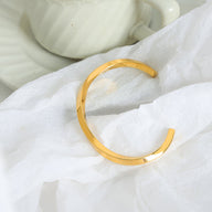 Bracelet jonc ouvert en titane plaqué or brillant au design minimaliste et lisse.