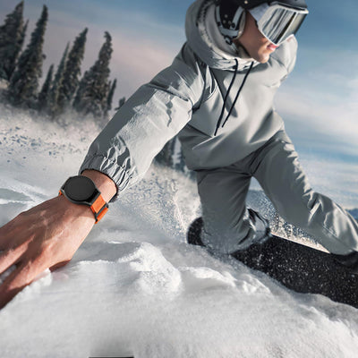 Bracelet sport en nylon orange avec fermoir velcro sur montre connectée noire, porté en snowboard.