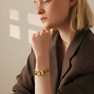 Bracelet boucle de ceinture en titane doré avec détails géométriques élégants porté au poignet féminin.