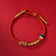 Bracelet serpent en fil rouge ciré avec détails dorés et perles colorées, design Tirzu.