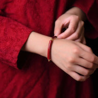 Bracelet en fil rouge ciré avec perles dorées porté au poignet, style minimaliste élégant.