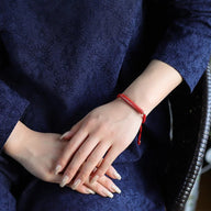 Bracelet en fil rouge ciré avec nœud coulissant, style minimaliste unisexe, porté au poignet.