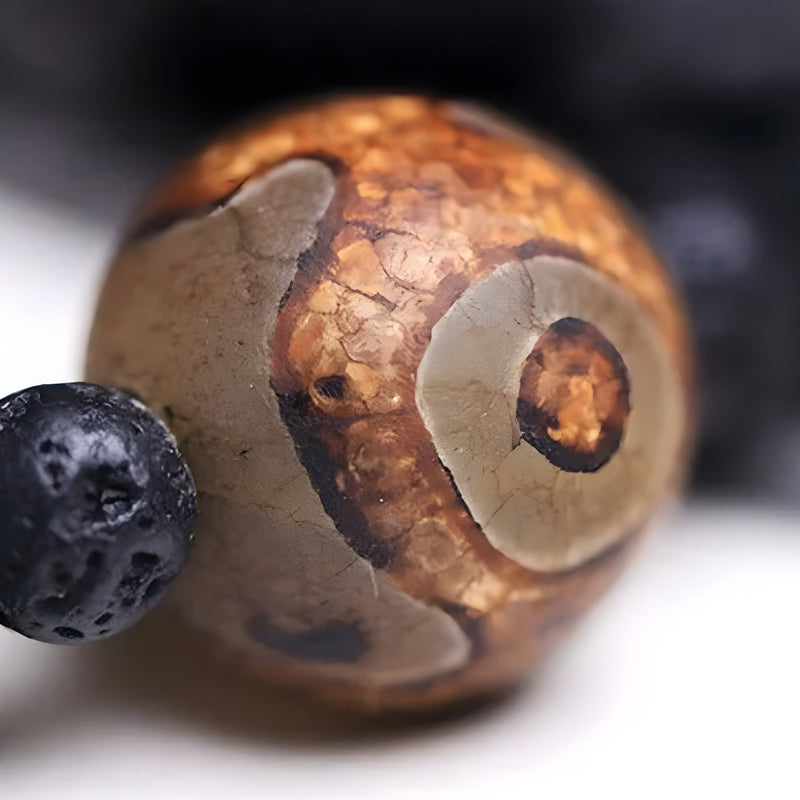 Perle de Dzi marron aux motifs circulaires avec perle noire en pierre volcanique cubique.