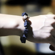 Bracelet tibétain noir en pierres volcaniques cubiques avec perle Dzi marron sur poignet clair.