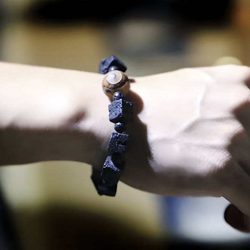 Bracelet tibétain noir en pierres volcaniques cubiques avec perle Dzi marron sur poignet clair.