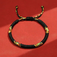 Bracelet tibétain en nylon noir tressé avec fils rouges, jaunes et verts, fermeture ajustable.