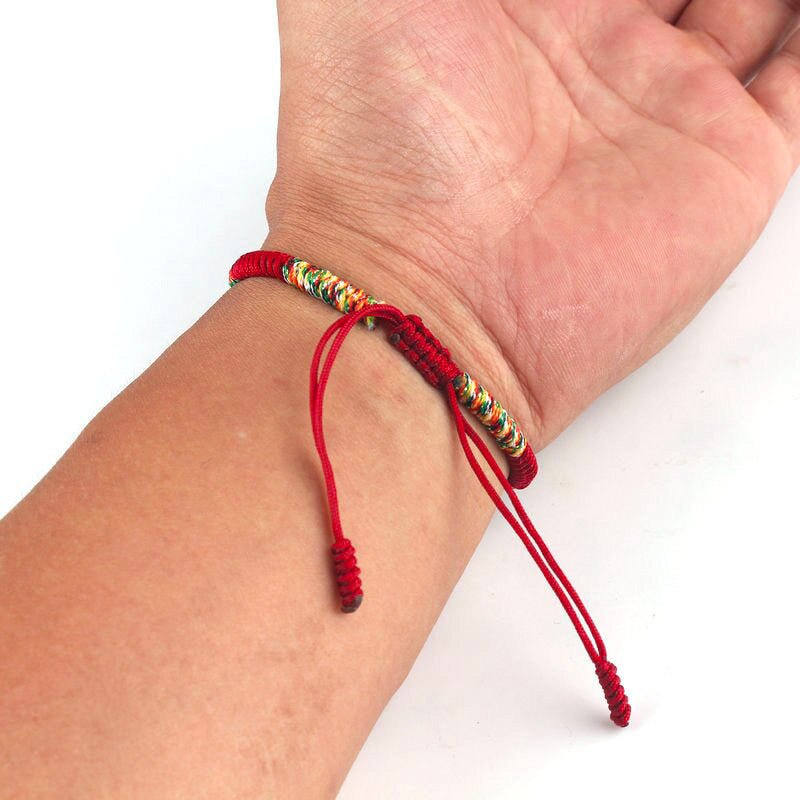 Bracelet tibétain en fil rouge noué avec perles dorées et fermeture coulissante ajustable.