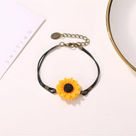 Bracelet noir en microfibre avec pendentif tournesol jaune et fermoir doré ajustable.