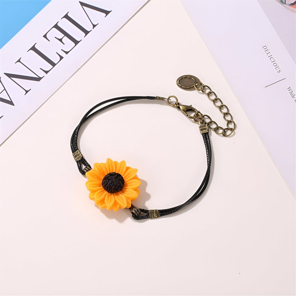 Bracelet noir en microfibre avec charm tournesol jaune et fermoir doré réglable.