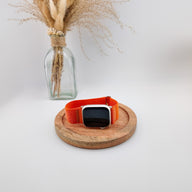 Bracelet Apple Watch en nylon orange vif avec fermeture velcro, style Trail Edition, posé sur un plateau en bois clair.