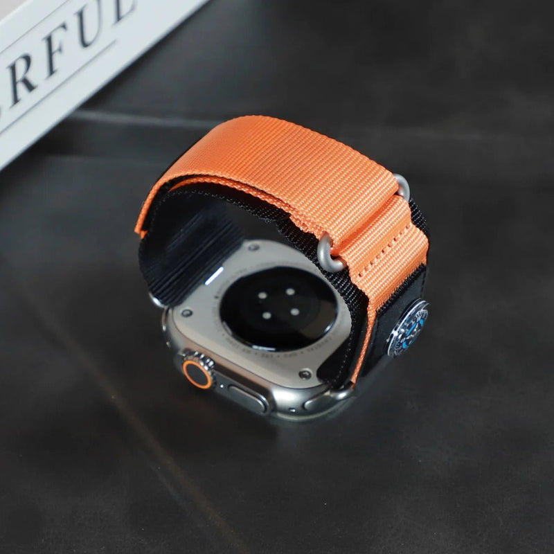 Bracelet tactique en nylon orange avec boussole intégrée, ajustable pour Apple Watch, dos en métal visible.