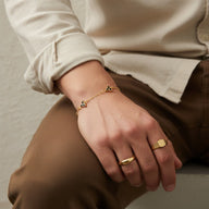 Bracelet fin doré avec un trèfle à trois feuilles stylisé, porté au poignet masculin, style chic et moderne.