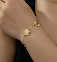 Bracelet en acier inoxydable doré avec pendentifs trèfle à cinq feuilles délicats sur poignet féminin.