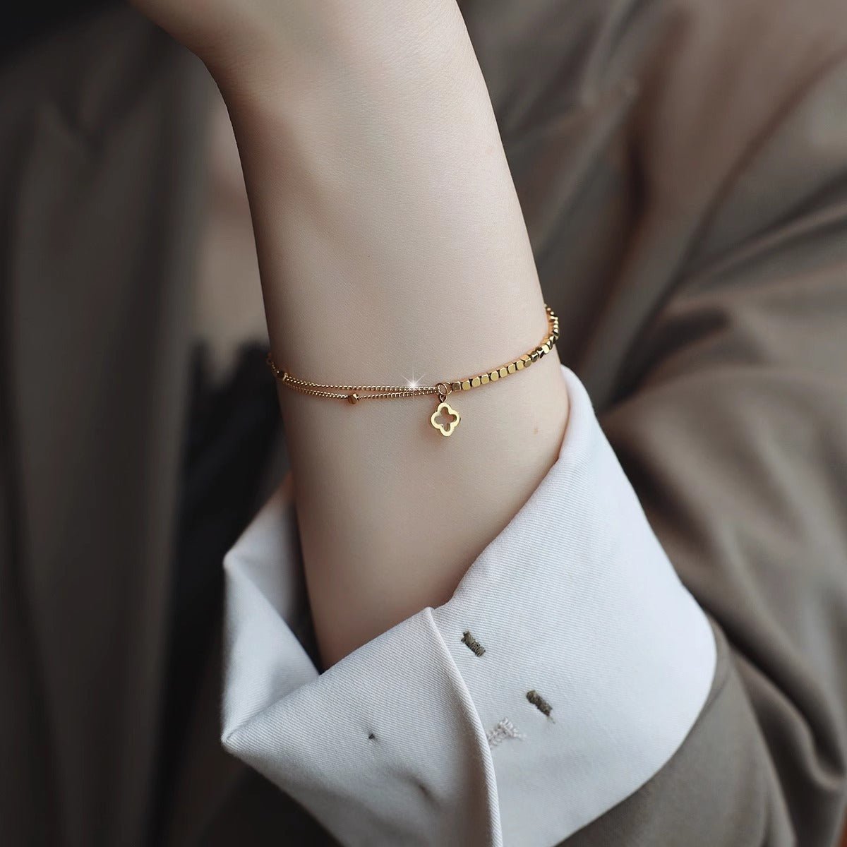 Bracelet doré double chaîne fine en titane avec pendentif trèfle porte-bonheur élégant, style minimaliste féminin.
