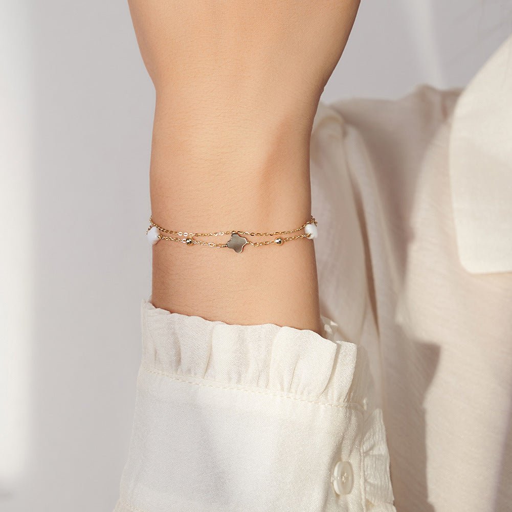 Bracelet double chaîne en argent 925 avec pendentifs trèfles en nacre blanche et noire, style délicat sur poignet féminin.