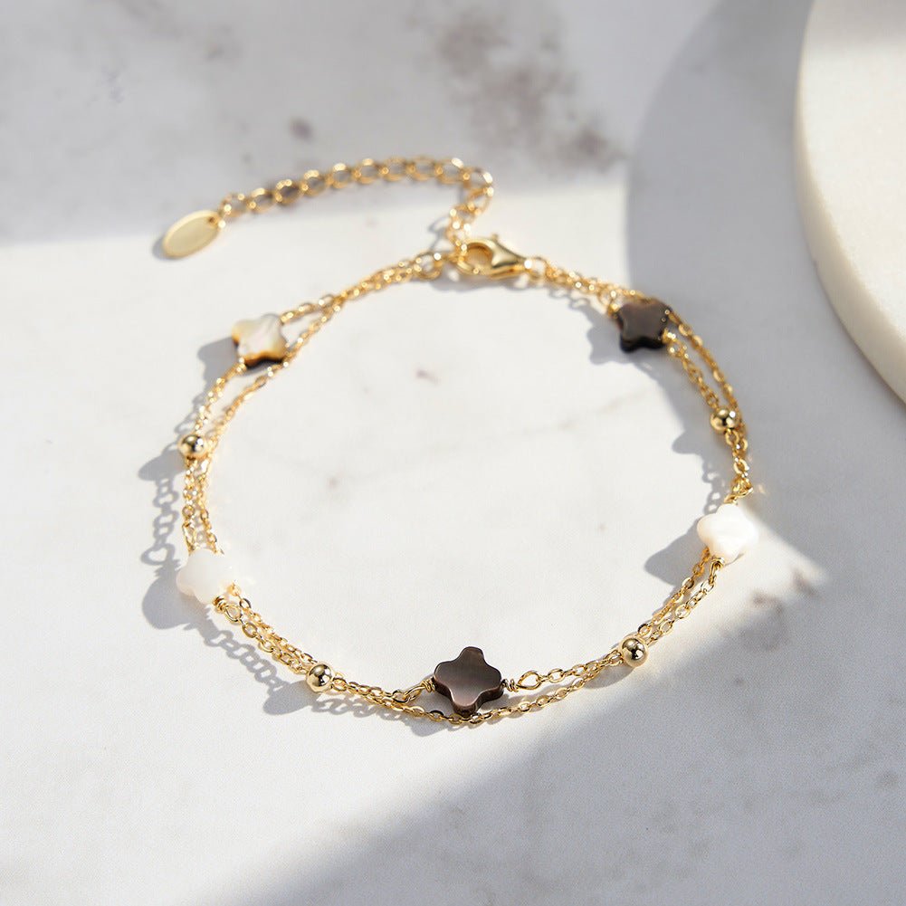 Bracelet double chaîne en argent doré avec quatre trèfles en nacre noire brillante, style délicat et raffiné.