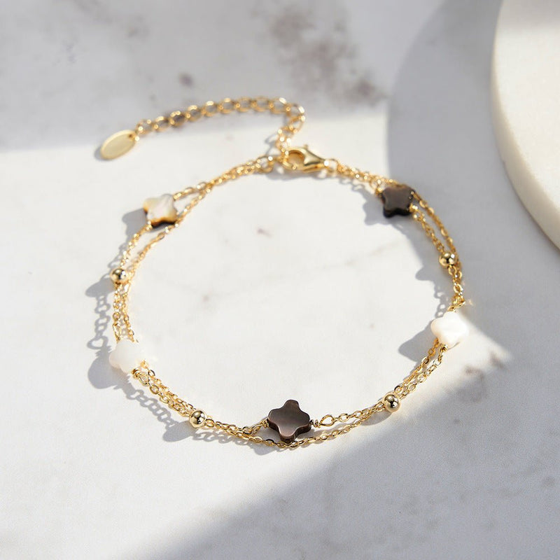 Bracelet double chaîne en argent doré avec quatre trèfles en nacre noire brillante, style délicat et raffiné.