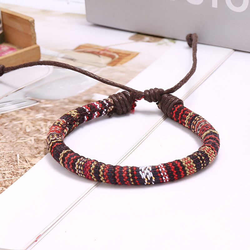 Bracelet tressé en coton aux motifs rouges, noirs et blancs avec fermoir ajustable en corde marron.
